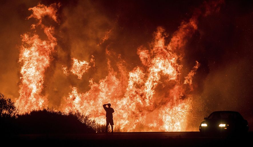 FILE - In this Dec. 6, 2017, file photo, a motorist on Highway 101 watches flames from the Thomas fire leap above the roadway north of Ventura, Calif. The largest wildfire recorded in California is officially out nearly six months after it began. Los Padres National Forest officials declared the Thomas fire extinguished Friday, June 1, 2018, after no hotspots were detected within the perimeter for more than two months. The fire broke out Dec. 4, 2017, near Thomas Aquinas College northwest of Los Angeles and burned more than 440 square miles. (AP Photo/Noah Berger, File)