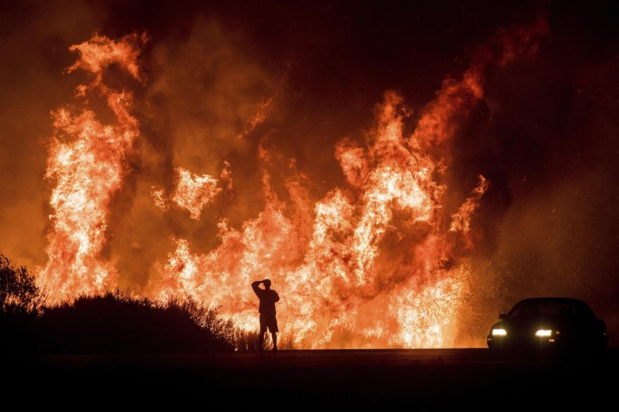 FILE - In this Dec. 6, 2017, file photo, a motorist on Highway 101 watches flames from the Thomas fire leap above the roadway north of Ventura, Calif. The largest wildfire recorded in California is officially out nearly six months after it began. Los Padres National Forest officials declared the Thomas fire extinguished Friday, June 1, 2018, after no hotspots were detected within the perimeter for more than two months. The fire broke out Dec. 4, 2017, near Thomas Aquinas College northwest of Los Angeles and burned more than 440 square miles. (AP Photo/Noah Berger, File)