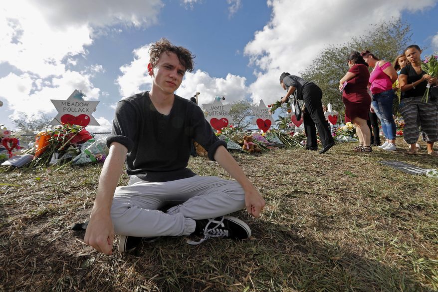 FILE- In this Feb. 19, 2018, file photo, Chris Grady, a student at Marjory Stoneman Douglas High School, sits at a memorial in Parkland, Fla., for those slain in the Feb. 14 school shooting. Grady who had planned to join the U.S. Army before the shooting, has withdrawn his enlistment and will now work for the March for Our Lives movement. (AP Photo/Gerald Herbert, File)