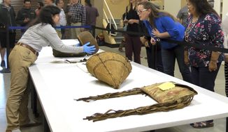 In this May 23, 2018, photo, Assistant Collections Manager for the British Museum Cynthia McGowan, left, handles a woven basket in Grand Ronde, Ore., that was collected from the Confederated Tribes of the Grand Ronde in the 1870s. Looking on are tribal chairwoman Cheryle Kennedy, right, tribal council member Kathleen George, center, and tribal attorneys Rob Greene and Jennifer Biesack. Tribal artifacts hidden away in the archives of the British Museum in London for nearly 120 years are being returned to the Oregon tribe from the British Museum and go on display Tuesday, June 5. (AP Photo/Gillian Flaccus)