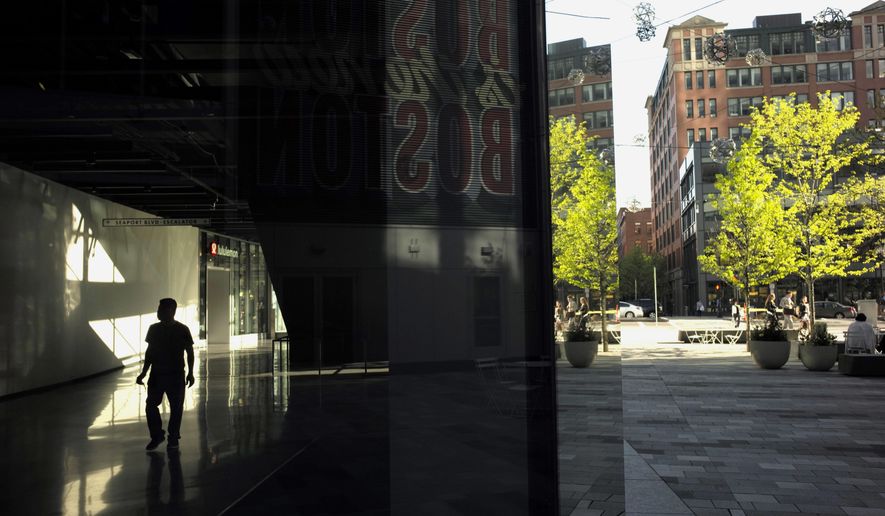 In this May 14, 2018 photo a passer-by walks through the lobby of a building in Boston's Seaport District. In this old city’s booming Seaport District, General Electric is building its new world headquarters, Amazon is bringing in thousands of new workers, and Reebok’s red delta symbol sits atop the new office it opened last year. Three businesses are testing self-driving cars, other dynamic companies are planting their flag, and trendy restaurants and apartments have gone up virtually overnight. But after bad flooding during a storm this past winter, critics wonder whether it was a bright idea to invest so much in a man-made peninsula that sits barely above sea level. (AP Photo/Steven Senne)