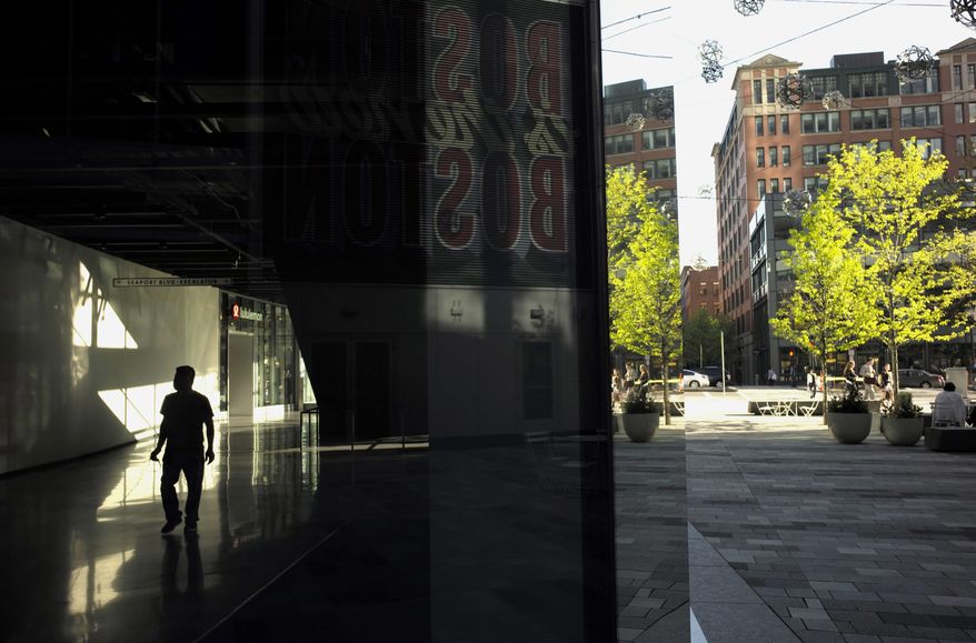 In this May 14, 2018 photo a passer-by walks through the lobby of a building in Boston's Seaport District. In this old city’s booming Seaport District, General Electric is building its new world headquarters, Amazon is bringing in thousands of new workers, and Reebok’s red delta symbol sits atop the new office it opened last year. Three businesses are testing self-driving cars, other dynamic companies are planting their flag, and trendy restaurants and apartments have gone up virtually overnight. But after bad flooding during a storm this past winter, critics wonder whether it was a bright idea to invest so much in a man-made peninsula that sits barely above sea level. (AP Photo/Steven Senne)