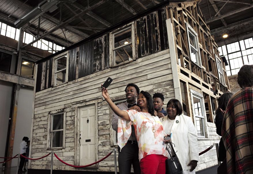 FILE - In this April 1, 2018 file photo, Cheryl Galloway, of Providence, R.I., uses a mobile phone to take a photo with family members in front of the rebuilt house of Rosa Parks at the WaterFire Arts Center in Providence, R.I. The house where Parks sought refuge in Detroit after fleeing the South will be auctioned after being turned into a work of art. Guernsey's auction house says the sale will be held mid-summer and that it's expected to fetch seven figures. (AP Photo/Steven Senne, File)