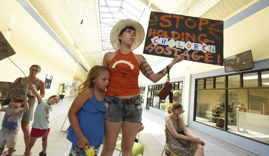 Amanda and Leighlou Reece hold up a protest sign as hundreds of Wilmington residents protest the Trump Administration's family separation policies during a Keep Families Together Rally outside of Rep. David Rouzer's office Wednesday June 20, 2018 at the New Hanover County Government Center in Wilmington, N.C. (Ken Blevins/The Star-News via AP)