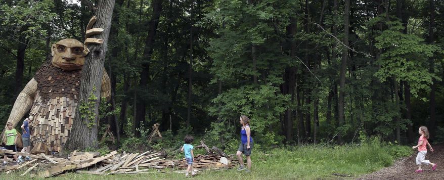 In this Thursday, June 14, 2018 photo, visitors get a close up view of one of the six larger than life trolls, guardians of the forest, at Morton Arboretum in Lisle, Ill. Danish artist Thomas Dambo and his team created the trolls using hundreds of pieces of reclaimed wood, battered boards, fallen trees and branches. Six colossal wooden trolls make their home in the Morton Arboretum's 1,700 acres. (Antonio Perez/Chicago Tribune via AP)