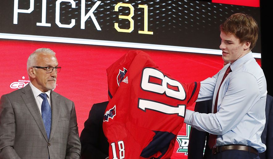 Alexander Alexeyev, right, of Russia, puts on a jersey after being selected by the Washington Capitals during the NHL hockey draft in Dallas, Friday, June 22, 2018. (AP Photo/Michael Ainsworth) ** FILE **