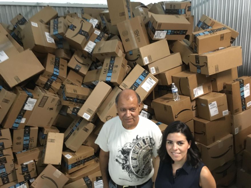 In this photograph taken June 24, 2018, Catholic Charities of the Rio Grande Valley staffer Eli Fernandez and volunteer Natalie Montelongo pose for a photo as they stand by a pile of unsorted Amazon boxes packed with donations in McAllen, Texas. A rest center for asylum-seekers in the Texas border town of McAllen has seen such a big surge of donations that they&#x27;ve had to rent additional storage space, and caravans of volunteers from across the U.S. have also showed up at their doors. (AP Photo/Manuel Valdes)