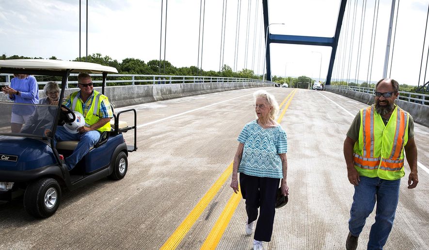 In this June 19, 2018 photo, Delores Evans, center, 94, walks across the top of the new Illinois 104 bridge over the Illinois River at Meredosia two hours before it was officially opened in Meredosia, Ill. Evans' home in Meredosia is just a few feet from the approach to the bridge and the offer to see it first hand came from Scott Halverson, left, of Halverson Construction, who says Evans put up with a lot during construction. It was a round-trip more than 80 years in the making when a single vehicle marked the first crossing of the new $86.2 million Illinois 104 bridge over the Illinois River at Meredosia (Rich Saal/The State Journal-Register via AP)