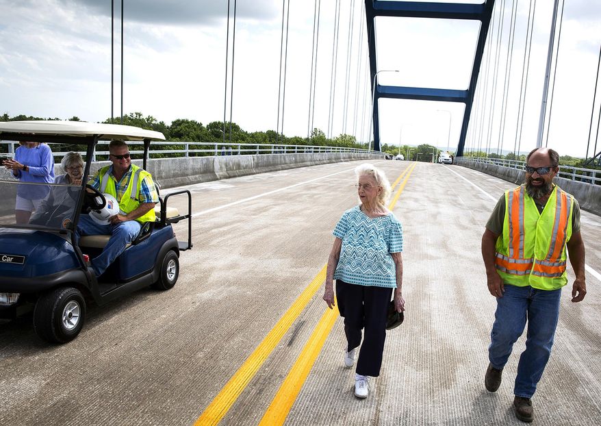 In this June 19, 2018 photo, Delores Evans, center, 94, walks across the top of the new Illinois 104 bridge over the Illinois River at Meredosia two hours before it was officially opened in Meredosia, Ill. Evans' home in Meredosia is just a few feet from the approach to the bridge and the offer to see it first hand came from Scott Halverson, left, of Halverson Construction, who says Evans put up with a lot during construction. It was a round-trip more than 80 years in the making when a single vehicle marked the first crossing of the new $86.2 million Illinois 104 bridge over the Illinois River at Meredosia (Rich Saal/The State Journal-Register via AP)