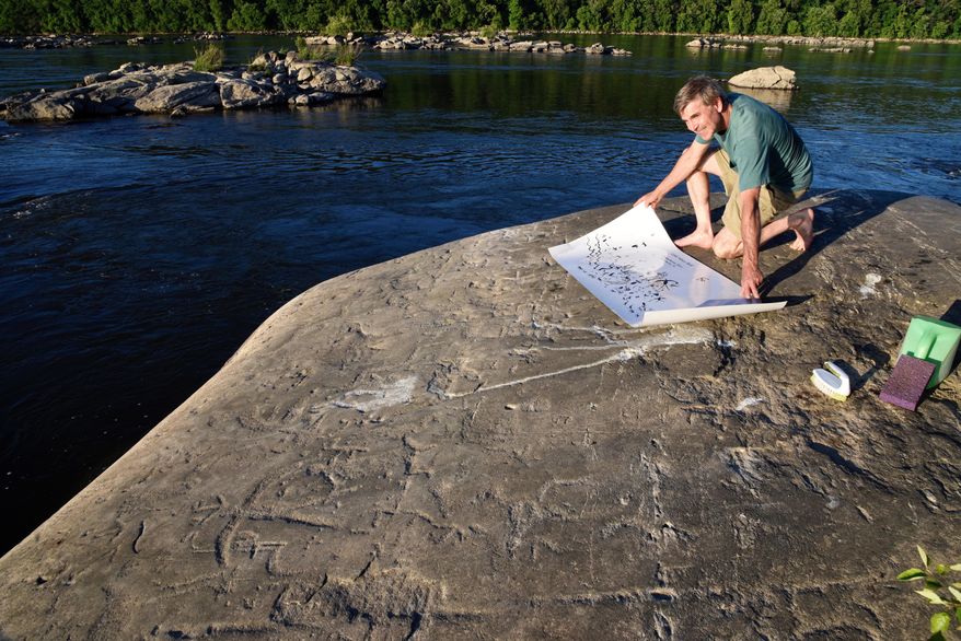 Paul Nevin, an expert on Native American petroglyphs, consults a map of about 150 carvings on Little Indian Rock on Tuesday, June 19, 2018, near the Safe Harbor Dam, Lancaster County, Pa. There are about 300 carvings on seven mica schist rocks amid a jumble of other rocks out here in the middle of the river. It is believed they were carved by Shenks Ferry Native Americans, using simple stone tools over a period from 500 to 1,000 years ago. (Ad Crable /LNP via AP)