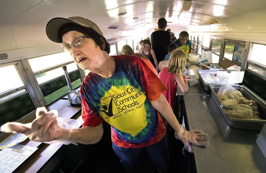 Food service worker Mary Hughes gestures for people to enter the vehicle Tuesday, June 5, 2018, at a new Sioux City Community Schools mobile food bus at Sioux City's Leeds Splash Pad. Children ages 1-18 have access to free lunch from the mobile food bus from 10:45-11:30 at the splash pad and from noon-12:45 pm at the LaunchPAD Children's Museum in downtown Sioux City. The free lunches are Monday-Friday through July 27. (Tim Hynds/Sioux City Journal via AP)