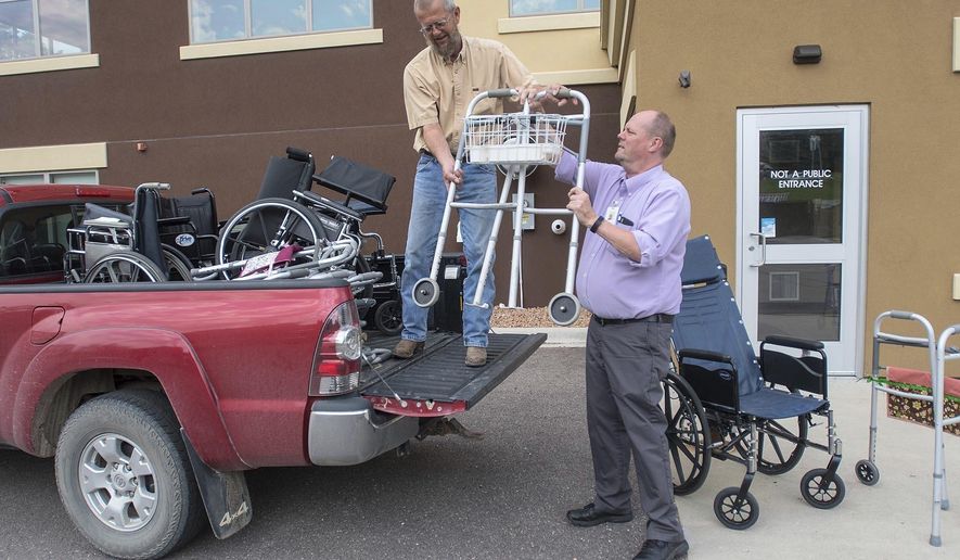 Gregg Olson, left, takes a walker from Mike Lagerquist of VINE Faith in Action outside the senior center's building Friday, June 15, 2018 in Mankato. Olson collects old walkers and wheelchairs until he has enough to fit a trailer, at which point he takes the haul to the Twin Cities where they are refurbished and sent to countries around the world for those in need of them. (Jackson Forderer/The Free Press via AP)