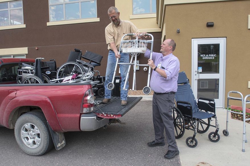 Gregg Olson, left, takes a walker from Mike Lagerquist of VINE Faith in Action outside the senior center's building Friday, June 15, 2018 in Mankato. Olson collects old walkers and wheelchairs until he has enough to fit a trailer, at which point he takes the haul to the Twin Cities where they are refurbished and sent to countries around the world for those in need of them. (Jackson Forderer/The Free Press via AP)