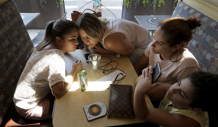 In this June 29, 2018, photo, Sirley Silveira Paixao, an immigrant from Brazil seeking asylum, left, and paralegal and interpreter Luana Mason listen on the phone to Denise Brown, director of Heartland Human Care Service, on the procedures Paixao needs to fulfill to get her son Diego released from immigration detention in Chicago. Seated with them are Lidia Karine Souza, second from right, and her son Diogo, who recently was released from immigration detention. Paixao and her son arrived in this country from Brazil on May 22, and were separated shortly after. She was released on June 13 and has been living in Massachusetts, while her son was taken to Chicago. (AP Photo/Charles Rex Arbogast)