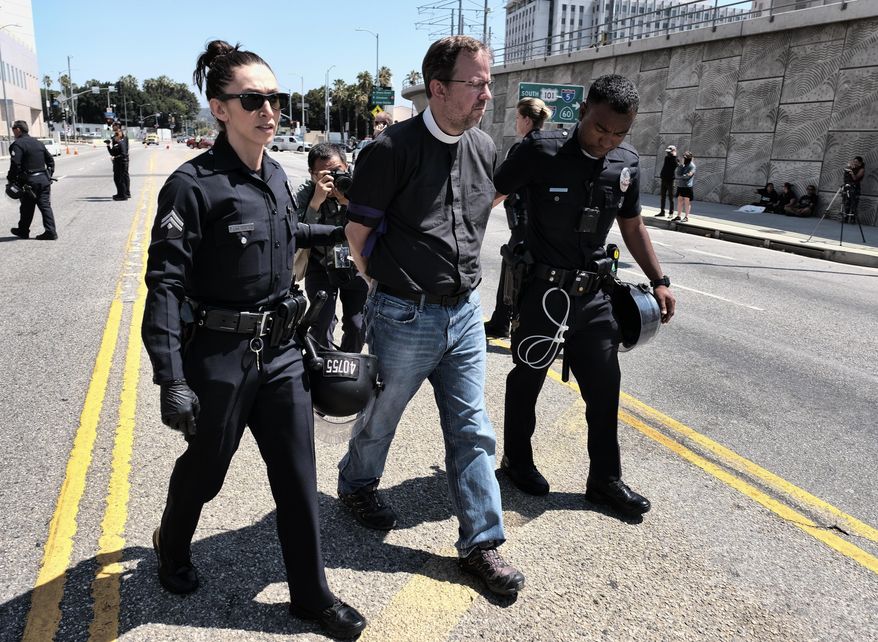 A member of the clergy is taken away in handcuffs after being arrested protesting in front of the Immigration and Customs Enforcement facility in downtown Los Angeles on Monday, July 2, 2018. A group of 17 protesters sat down in the street, blocking the entrance to the ICE facility Monday morning. (AP Photo/Richard Vogel)
