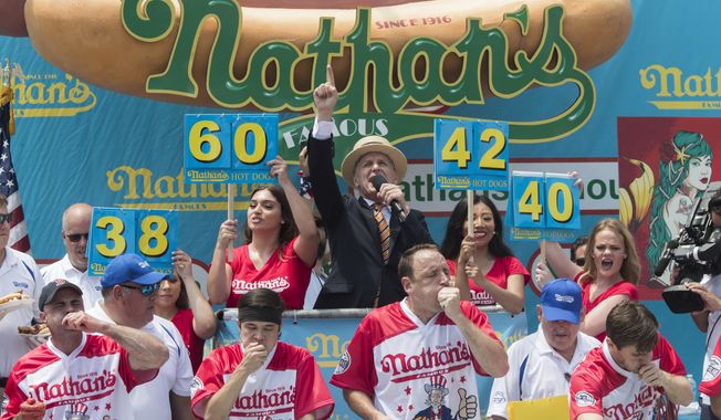 Master of Ceremony George Shea, top center, announces that reigning champion Joey Chestnut, bottom center, is winning the men&#x27;s competition of the Nathan&#x27;s Famous Fourth of July hot dog eating contest in the final seconds of the competition, Wednesday, July 4, 2018, in New York&#x27;s Coney Island. Chestnut broke his own world record by eating 74 hot dogs in 10 minutes. (AP Photo/Mary Altaffer)