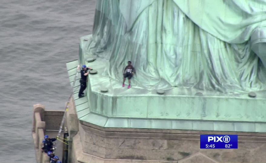 In this image made from video by PIX11, a person, center, leans against the robes of the Statue of Liberty on Liberty Island, as one of the police officers climbed up on a ladder to stand on a ledge nearby talking the climber into descending in New York, Wednesday, July 4, 2018. (PIX11 via AP)