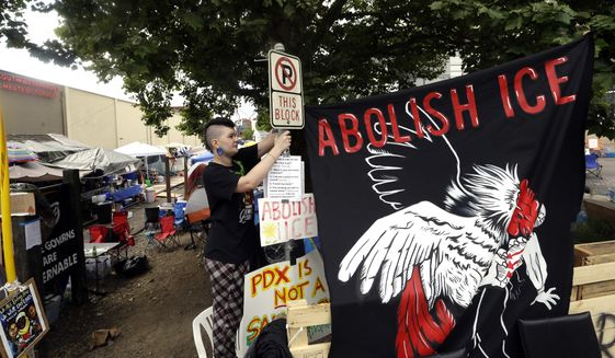 In this June 25, 2018, file photo, a woman, who would not identify herself, hangs a sign at a protest camp on property outside the U.S. Immigration and Customs Enforcement office in Portland, Ore. (AP Photo/Don Ryan, File)