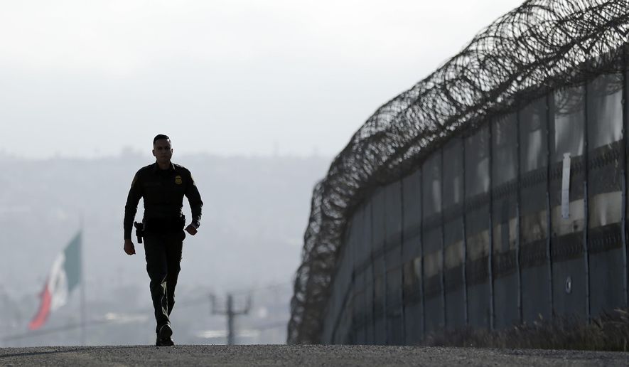 In this June 22, 2016, file photo, Border Patrol agent Eduardo Olmos walks near the secondary fence separating Tijuana, Mexico, background, and San Diego in San Diego. (AP Photo/Gregory Bull, File)