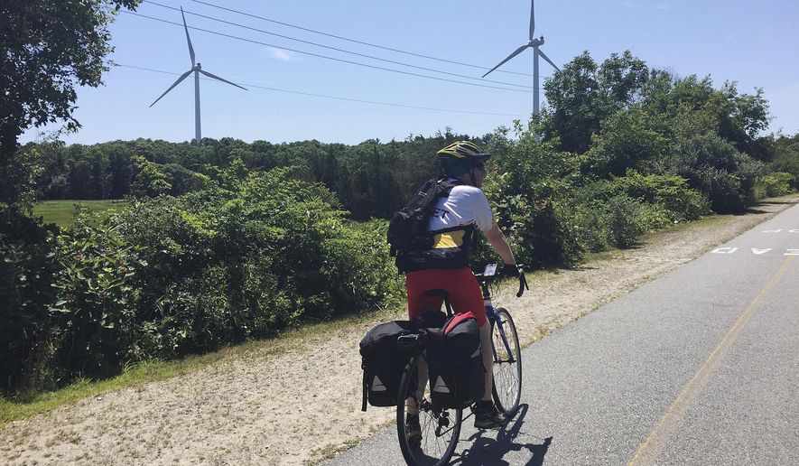 In this Friday, July 13, 2018 photo provided by Lori Riley, Associated Press reporter Pat Eaton-Robb rides past windmills on the Phoenix Trail in Fairhaven, Mass. The trail is part of the East Coast Greenway, a planned 3,000-mile collection of trails from Maine to Florida which is about 41 percent complete in southern New England. (Lori Riley via AP)