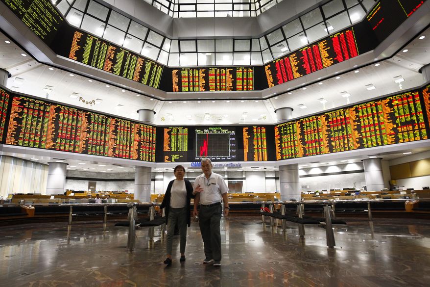 Investors walk in front of trading boards at a private stock market gallery in Kuala Lumpur, Tuesday, July 24, 2018. Asian markets rose on Tuesday as better-than-expected U.S. corporate earnings and the lack of bad news on trade tensions encouraged investors. (AP Photo/Vincent Thian)