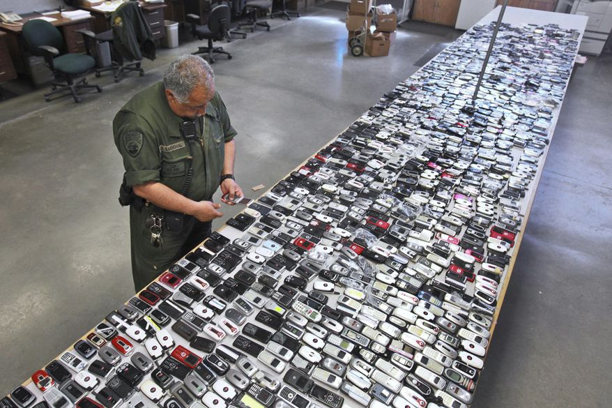 FILE - In this April 10, 2009, file photo, Correctional Officer Jose Sandoval inspects one of the more than 2,000 cell phones confiscated from inmates at California State Prison, Solano in Vacaville, Calif. Judges in California and South Carolina have ordered cellphone carriers to shut down nearly 200 contraband phones used by inmates in state prisons to coordinate drug deals, gang operations and even murders. California's corrections chief tells The Associated Press on Monday, July 23, 2018, that it's the first time prison officials obtained warrants requiring a mass shutdown of contraband phones. (AP Photo/Rich Pedroncelli, File)