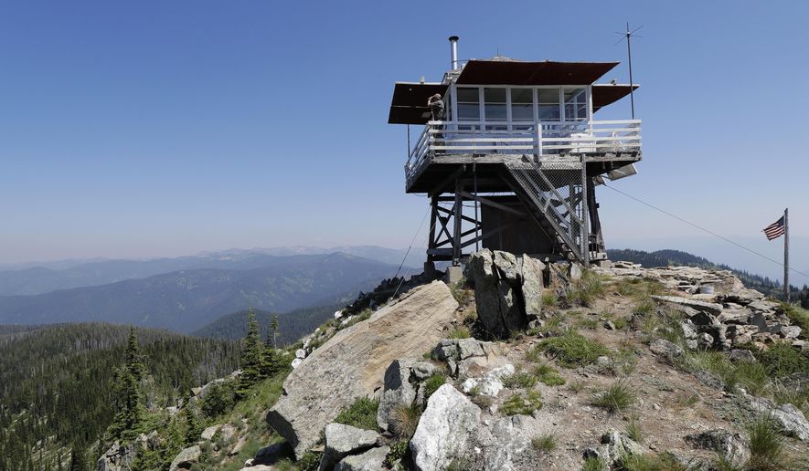 In this Wednesday, July 18, 2018, photo, Tom VandeWater stands at the railing of the Coolwater Fire Lookout and looks through his binoculars in the Nez Perce-Clearwater National Forests near Lowell, Idaho. VandeWater, from Canton, N.Y., has staffed the lookout each summer for many years for the U.S. Forest Service. (AP Photo/Ted S. Warren)