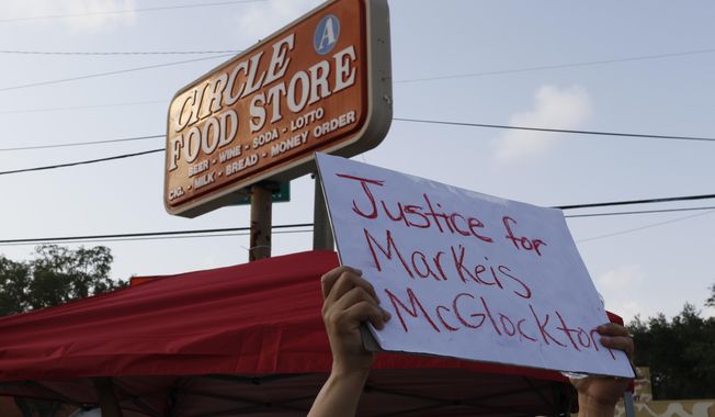 In this Sunday, July 22, 2018 photo, family, friends and demonstrators hold up signs in a parking lot in Clearwater, Fla., where Markeis McGlockton, 28, was shot and killed in an altercation. The family of McGlockton issued an appeal through their attorney for the public to put pressure on State Attorney Bernie McCabe to file charges against Michael Drejka, who fatally shot the father of three last Thursday during an argument over a handicapped parking space outside a convenience store. (Luis Santana/Tampa Bay Times via AP)