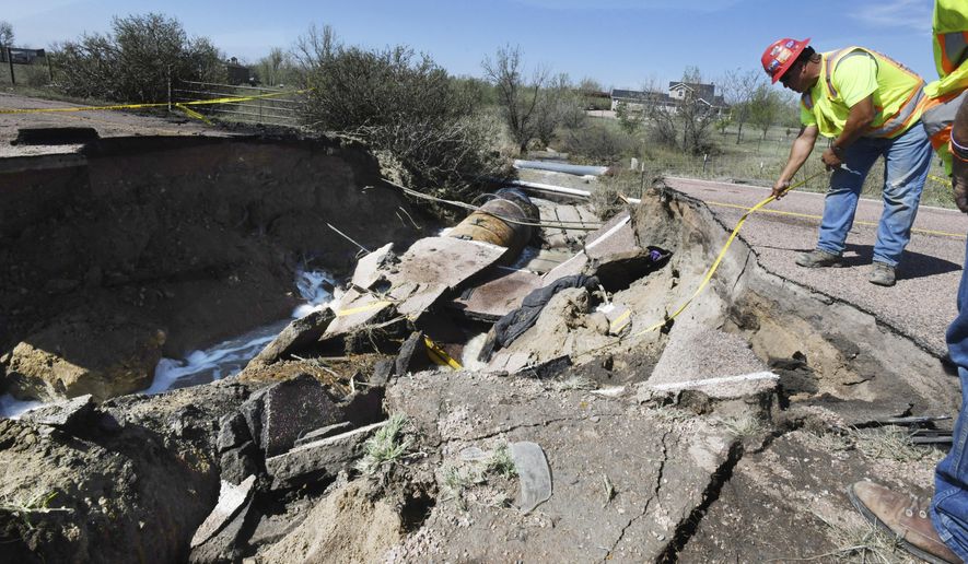 Utility worker Dino Rodriguez measures 16 feet to the bottom of a hole that was created in Old Pueblo Rd. south of Fountain, Colo., Tuesday, July 24, 2018. The massive hole happened after rain flooded the road during Monday's storm. A vehicle fell into the culvert and when the Hanover Fire Dept. responded to the cave-in, their fire truck fell into the hole on Tuesday. Both vehicles were removed early Tuesday morning. Two firefighters were injured and one person was airlifted from the scene. (Jerilee Bennett/The Gazette via AP)