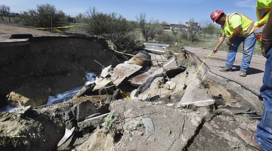 Utility worker Dino Rodriguez measures 16 feet to the bottom of a hole that was created in Old Pueblo Rd. south of Fountain, Colo., Tuesday, July 24, 2018. The massive hole happened after rain flooded the road during Monday's storm. A vehicle fell into the culvert and when the Hanover Fire Dept. responded to the cave-in, their fire truck fell into the hole on Tuesday. Both vehicles were removed early Tuesday morning. Two firefighters were injured and one person was airlifted from the scene. (Jerilee Bennett/The Gazette via AP)