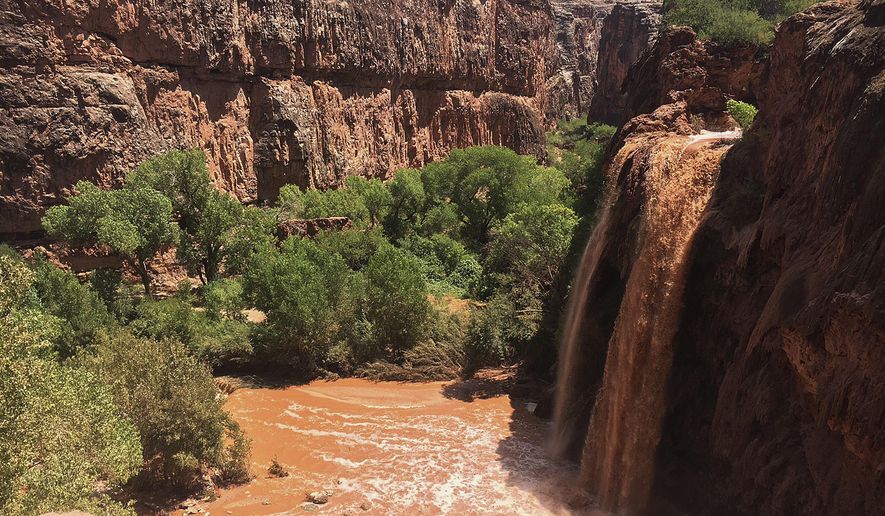This Wednesday, July 11, 2018 photo provided by Eric Kremer shows waterfalls normally blue-green turning muddy brown in Supai, Ariz., after flooding the area. Hundreds of tourists who booked coveted overnight trips on tribal land deep in a gorge off the Grand Canyon will have to reschedule after heavy flooding forced evacuations and shut down the area for at least a week. (Eric Kremer via AP)