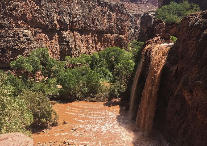 This Wednesday, July 11, 2018 photo provided by Eric Kremer shows waterfalls normally blue-green turning muddy brown in Supai, Ariz., after flooding the area. Hundreds of tourists who booked coveted overnight trips on tribal land deep in a gorge off the Grand Canyon will have to reschedule after heavy flooding forced evacuations and shut down the area for at least a week. (Eric Kremer via AP)