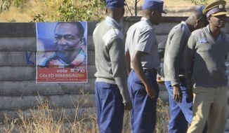 Zimbabwe police officers stand next to a campaign poster of Zimbabwean President Emmerson Mnangagwa at Nelson Chamisa&#39;s rally in Chitungwiza about 30 kilometres east of the capital Harare, Thursday, July, 26, 2018. Chamisa addressed his first rally since rejecting the idea of boycotting elections on Monday despite what he calls a biased election commission, in the first election since the November resignation of longtime leader Robert Mugabe. (AP Photo/Tsvangirayi Mukwazhi)