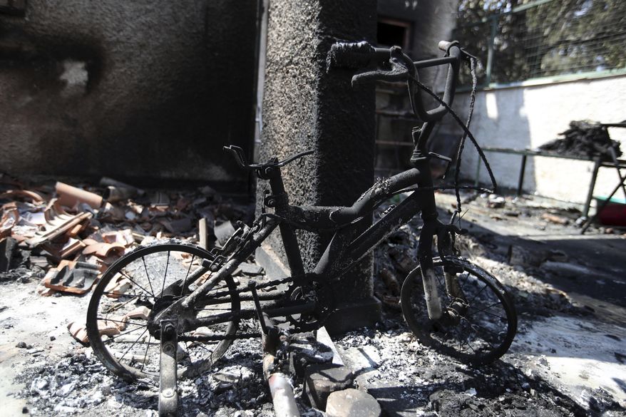 In this Wednesday, July 25, 2018 photo, a burnt bicycle with training wheels stands at the balcony of a destroyed house in Mati, east of Athens. More than 86 people were either killed by the flames or drowned on Monday's wildfire as they tried to flee the fire into the nearby sea, waiting for hours in the water for rescue from local fishermen and private boat owners who saved many. (AP Photo/Thanassis Stavrakis)