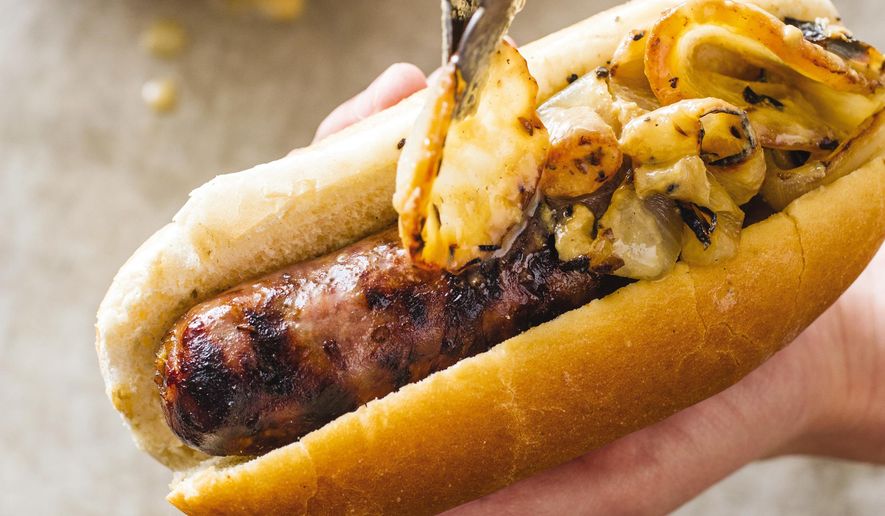 This undated photo provided by America's Test Kitchen in July 2018 shows grilled sausage with onions in Brookline, Mass. This recipe appears in the cookbook “Master of the Grill.” (Carl Tremblay/America's Test Kitchen via AP)