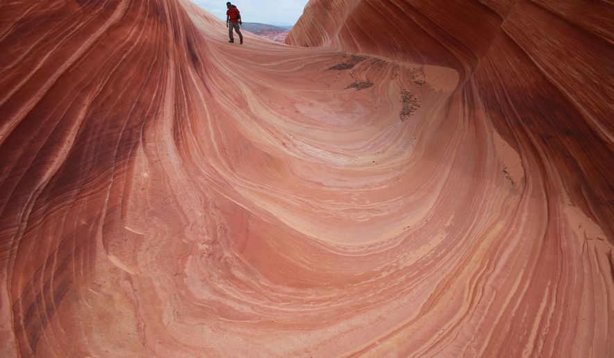 FILE - In this May 28, 2013, file photo, a hiker walks on a rock formation known as The Wave in the Vermilion Cliffs National Monument in Arizona. A 49-year-old Belgium man has died in an apparent heat-related death while hiking a popular spot near the Utah-Arizona border called "The Wave." Kane County Sheriff's Sgt. Alan Alldredge said Christophe Pochic was found dead Monday, July 30, 2018, after his 16-year-old son called his mom who was in a hotel to tell her that his father had become disoriented and needed help. The family was visiting Utah. (AP Photo/Brian Witte, File)