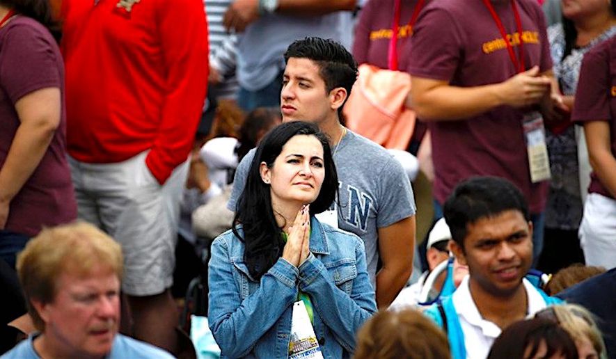 A woman holds her hands in prayer as she watches Pope Francis on a  monitor as people await his arrival on Sept. 26, 2015, in Philadelphia. (Associated Press)