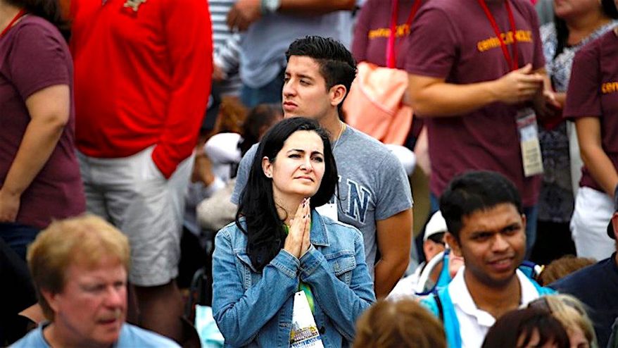 A woman holds her hands in prayer as she watches Pope Francis on a monitor as people await his arrival on Sept. 26, 2015, in Philadelphia. (Associated Press)