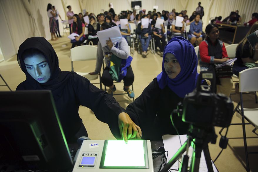 A government employee, left, takes the fingerprints of a foreign worker at a visa processing center in Al Aweer, about 30 kms, 18.6 miles, east of Dubai, United Arab Emirates, Wednesday, Aug. 1, 2018. The UAE has begun a three-month visa amnesty program hoping to resolve a Catch 22 situation for foreign workers who are fined daily for overstaying the time allowed, but cannot leave the Gulf nation until they have paid the penalties they owe. (AP Photo/Kamran Jebreili)