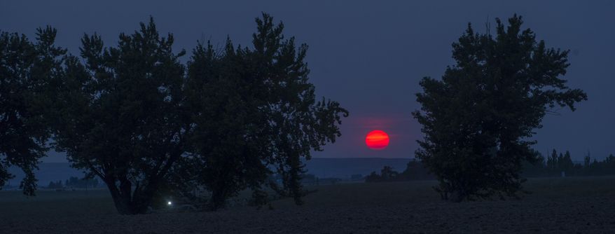 In this Monday, July 30, 2018 photo, with a sky full of wildfire smoke and haze, the sun set bright red south of Touchet, Wash. (Greg Lehman/Walla Walla Union-Bulletin via AP)
