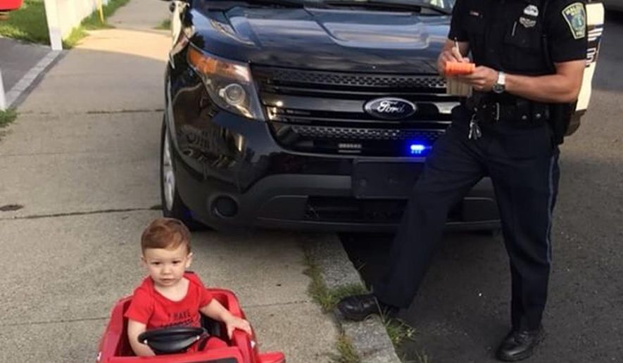 In this July 31, 2018 photo, Grayson Salerno, 1, is pulled over for driving without a license, but he got off with a "cuteness warning" in Malden, Mass. Police in the Boston suburb said they staged the traffic stop after spotting Salerno driving a red toy Mercedes convertible along a sidewalk. (Cori-Devan Salerno via AP)