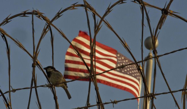 In this June 5, 2018 photo reviewed by U.S. military officials, a bird perches on barbed wire where a U.S. flag flies at the Camp VI detention facility on the Guantanamo Bay U.S. naval base in Cuba. The two Guantanamos have been a contrast since the U.S. opened the base at the southeastern tip of the island in 1903, following the Spanish-American War, and the divide has only grown under Cuba&#x27;s communist government, which refuses to cash the annual rent checks from Washington as it insists the U.S. leave. (AP Photo/Ramon Espinosa)