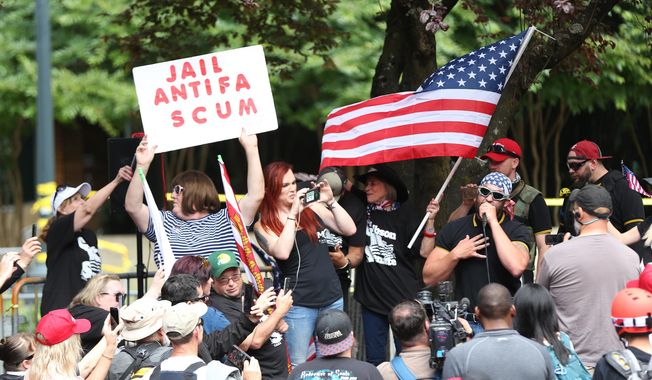 FILE--In this June 30, 2018, file photo, the Patriot Prayer group holds a rally and march in Portland, Ore., amid a protest by anti-fascist groups. Portland is bracing for what could be another round of violent clashes Saturday, Aug. 4, 2018, between a right-wing group holding a rally here and self-described anti-fascist counter-protesters who have pledged to keep Patriot Prayer and other affiliated groups out of this ultra-liberal city. (Mark Graves/The Oregonian via AP, file)
