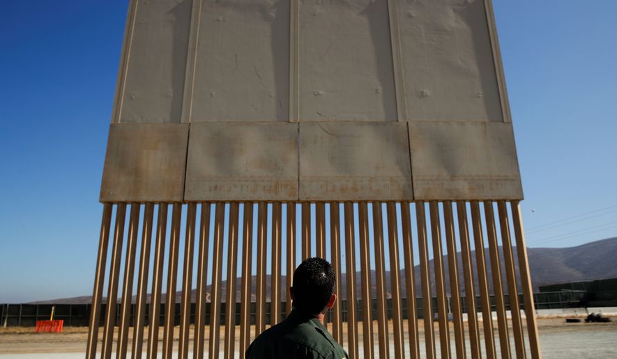A U.S. Border Patrol agent looks at one of border wall prototypes Thursday, June 28, 2018, in San Diego. (AP Photo/Jae C. Hong)