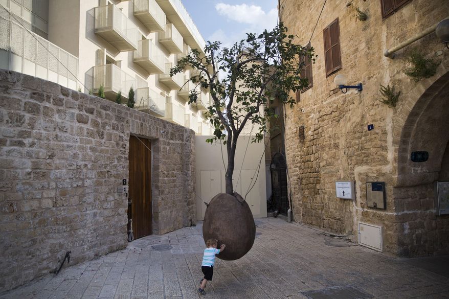 In this Saturday, July 28, 2018 photo, a child plays next to a 100-year-old orange tree hanging above the ground in the old city of Jaffa, Israel. Israel's port city of Jaffa is an ancient place. Today glass towers and modern apartment complexes rise amid Jaffa's old white stone buildings. It's famous for its flea market and hummus cafes. But visitors will also find trendy bars, galleries and boutiques. (AP Photo/Oded Balilty)