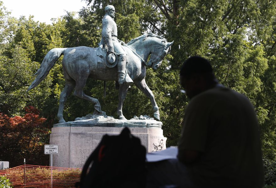 In this Monday, Aug. 6, 2018, photo, a visitor eats lunch in front of a statue of Robert E. Lee that is surrounded by fencing and a No Trespassing sign in Charlottesville, Va., at the park that was the focus of the Unite the Right rally. (AP Photo/Steve Helber)