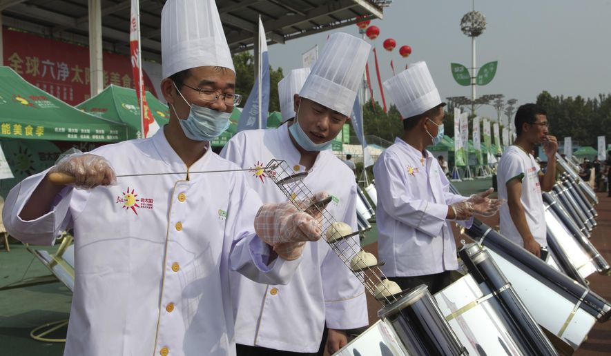 In this photo taken Thursday, Aug. 2, 2018, chefs prepare to cook buns in a solar cooker that using a metal and glass vacuum tube heated by mirrors curved to capture the sun's heat in Dezhou in the eastern Shandong province in China. Two dozen chefs with white aprons and hats cooked soups, baked buns, potatoes, and boiled rice at a festival to demonstrate the potential of solar cookers that organizers claim can help reduce climate-changing greenhouse gas emissions. (AP Photo/Fu Ting)