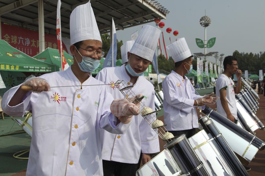 In this photo taken Thursday, Aug. 2, 2018, chefs prepare to cook buns in a solar cooker that using a metal and glass vacuum tube heated by mirrors curved to capture the sun's heat in Dezhou in the eastern Shandong province in China. Two dozen chefs with white aprons and hats cooked soups, baked buns, potatoes, and boiled rice at a festival to demonstrate the potential of solar cookers that organizers claim can help reduce climate-changing greenhouse gas emissions. (AP Photo/Fu Ting)