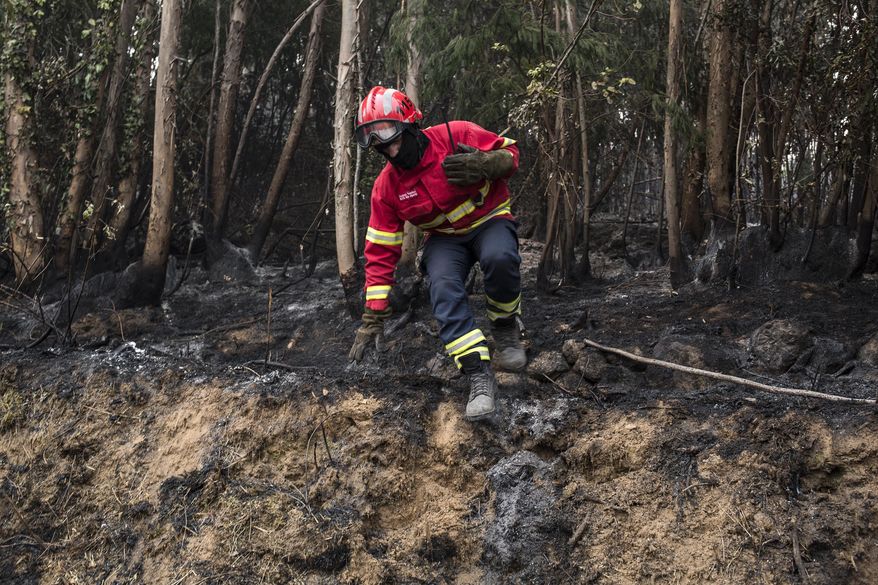 A firefighter jumps off a small mound while working on a fire near the village of Monchique, in southern Portugal's Algarve region, Monday, Aug. 6, 2018. Emergency services in Portugal say they are still fighting a major wildfire on the south coast that threatened to engulf a hillside town overnight. (AP Photo/Javier Fergo)