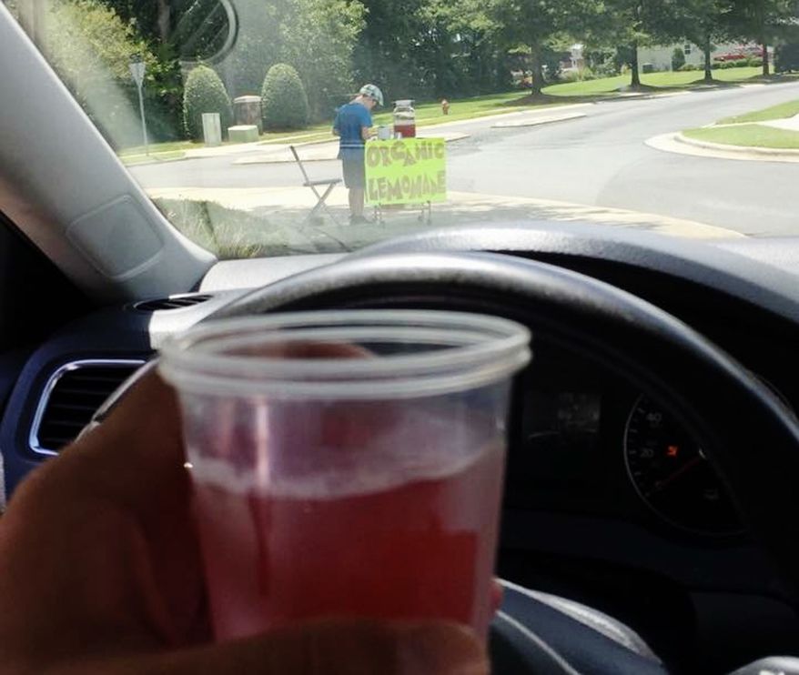 CORRECTS TO A BOY, NOT A TEENAGER - This Saturday, Aug. 4 2018, photo provided by James Castellano, of Monroe, N.C., shows a drink he bought from a boy, background, in Monroe. A teenager who held up the North Carolina lemonade stand for $17 was still at large Monday, Aug. 6, and authorities said they hoped to track him through surveillance footage and possible DNA and fingerprint tests. (James Castellano via AP)